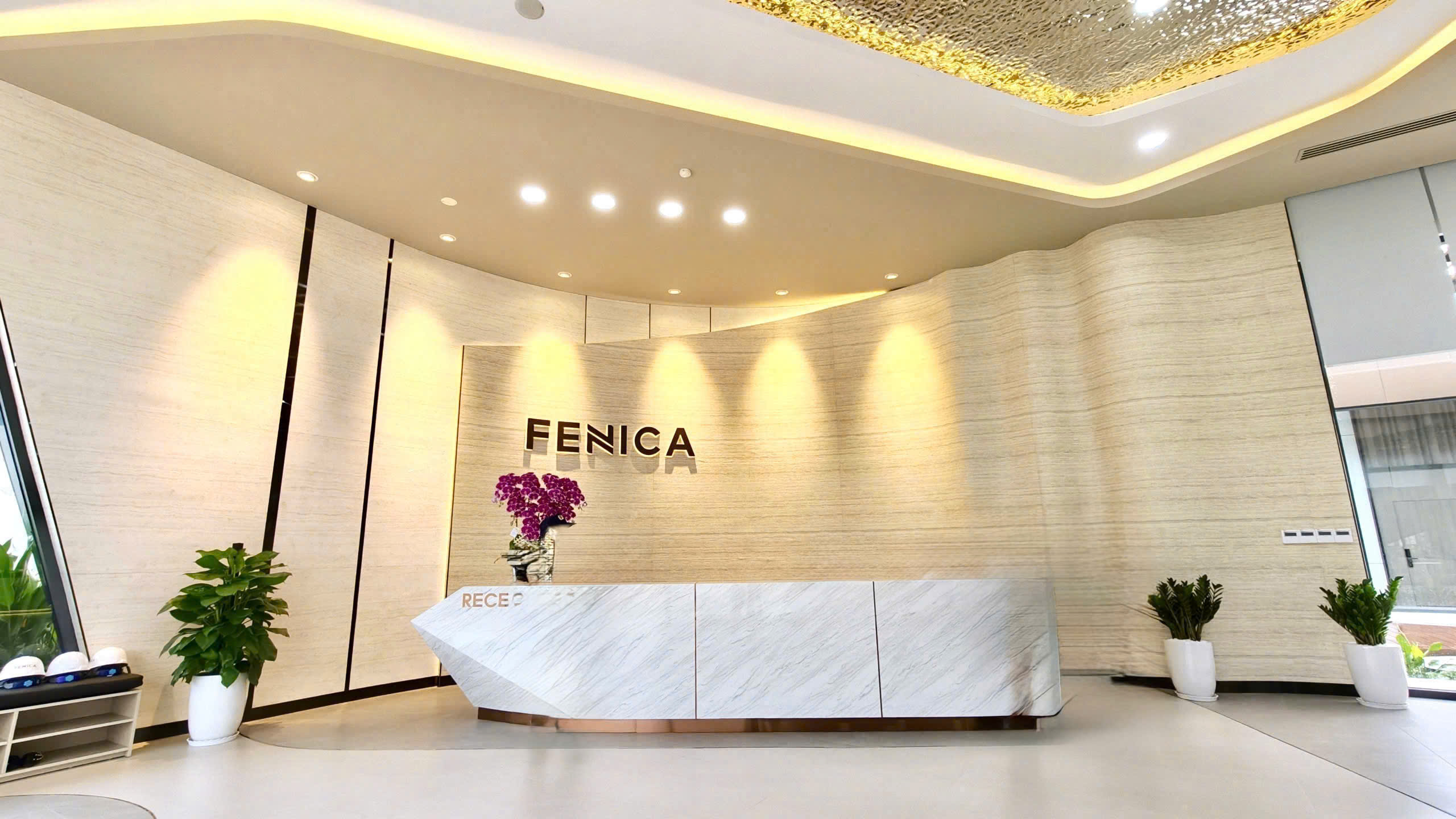 Sảnh lễ tân Fenica ốp đá marble, trần thả đèn vàng ánh kim, bàn tiếp tân khắc chữ FENICA